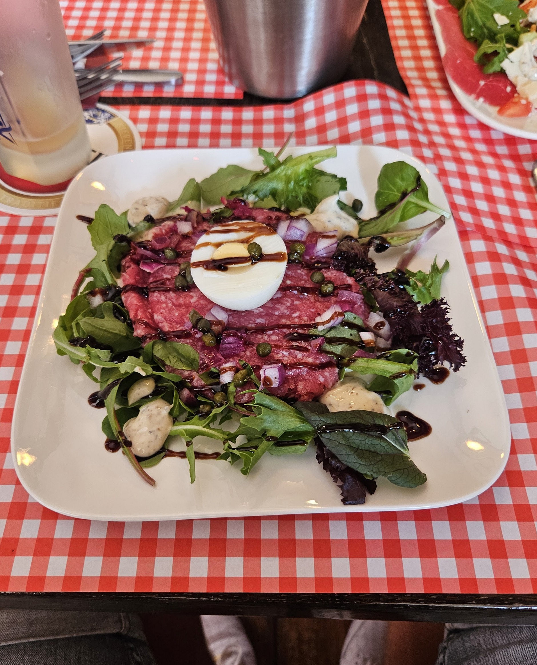 Carpaccio op een wit bord, met ei en salade